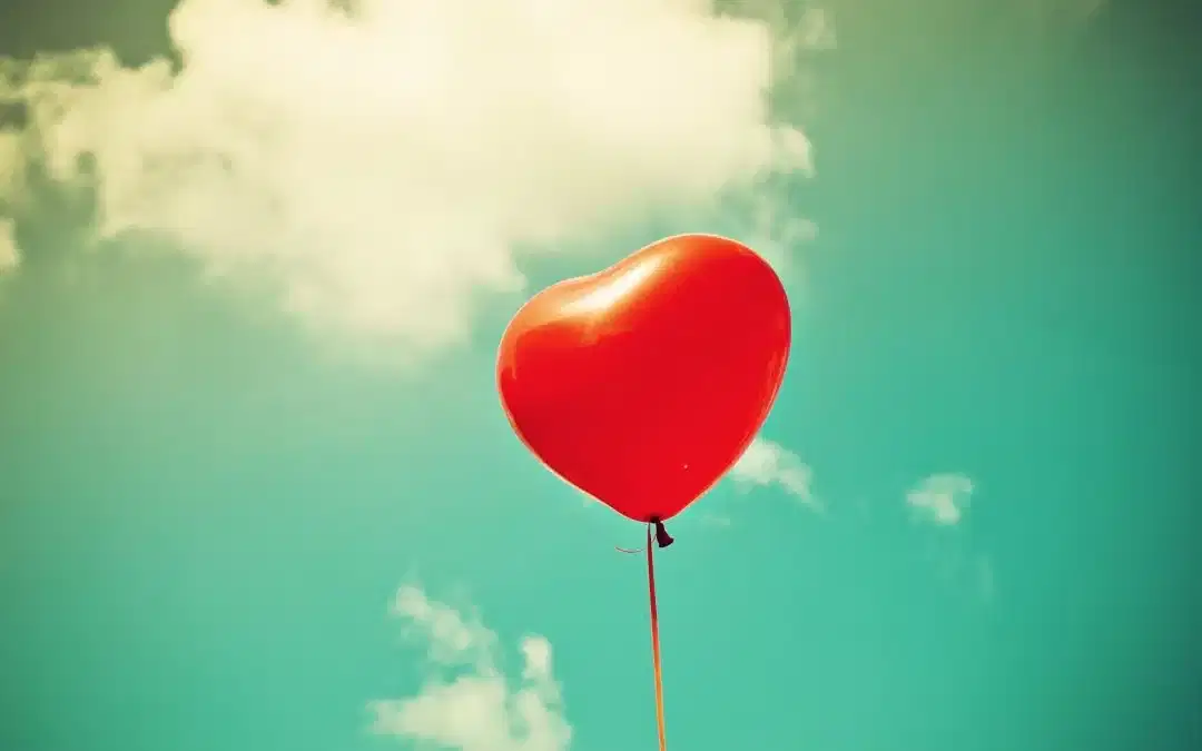 Red balloon floating in cloudy blue sky